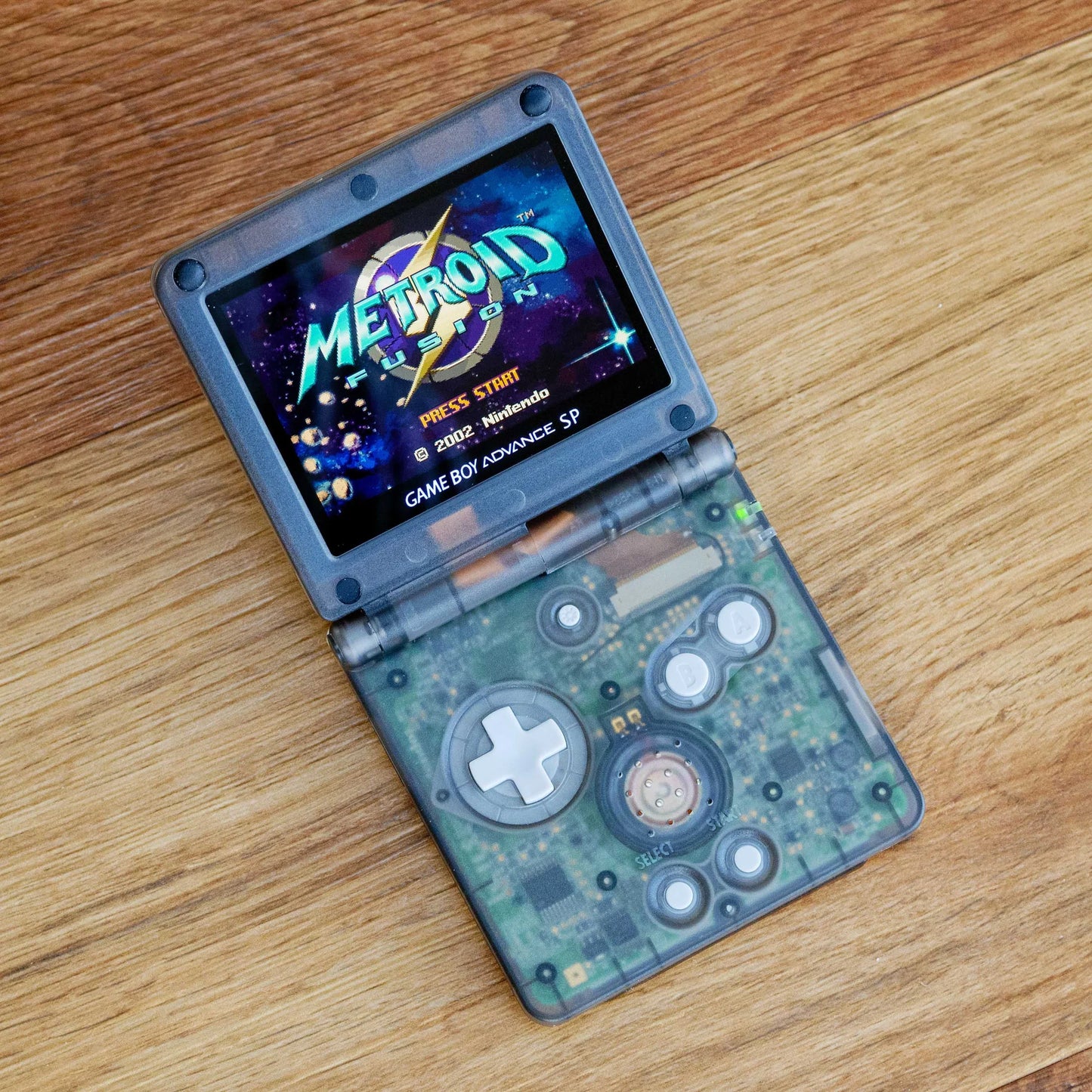 GBA SP Handheld gaming console displaying 'Metroid' on a wooden surface robot retro
