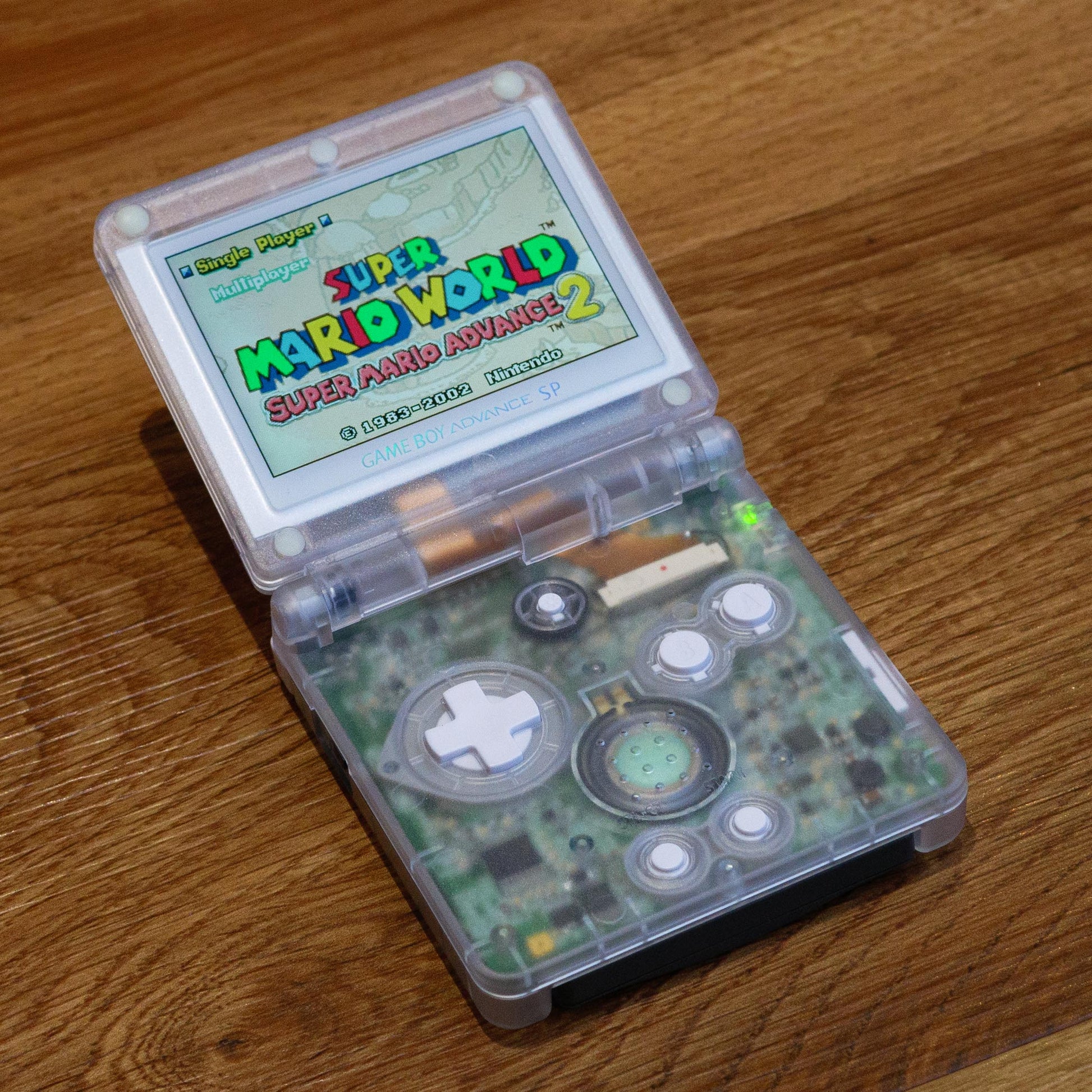 GBA SP Handheld gaming console displaying 'Super Mario World' on a wooden surface robot retro