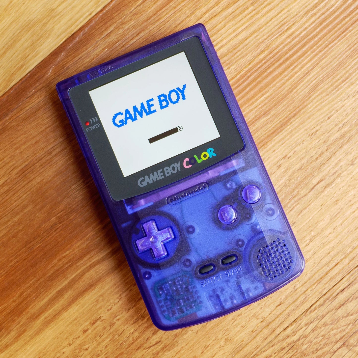 Purple Game Boy Color on a wooden surface robot retro